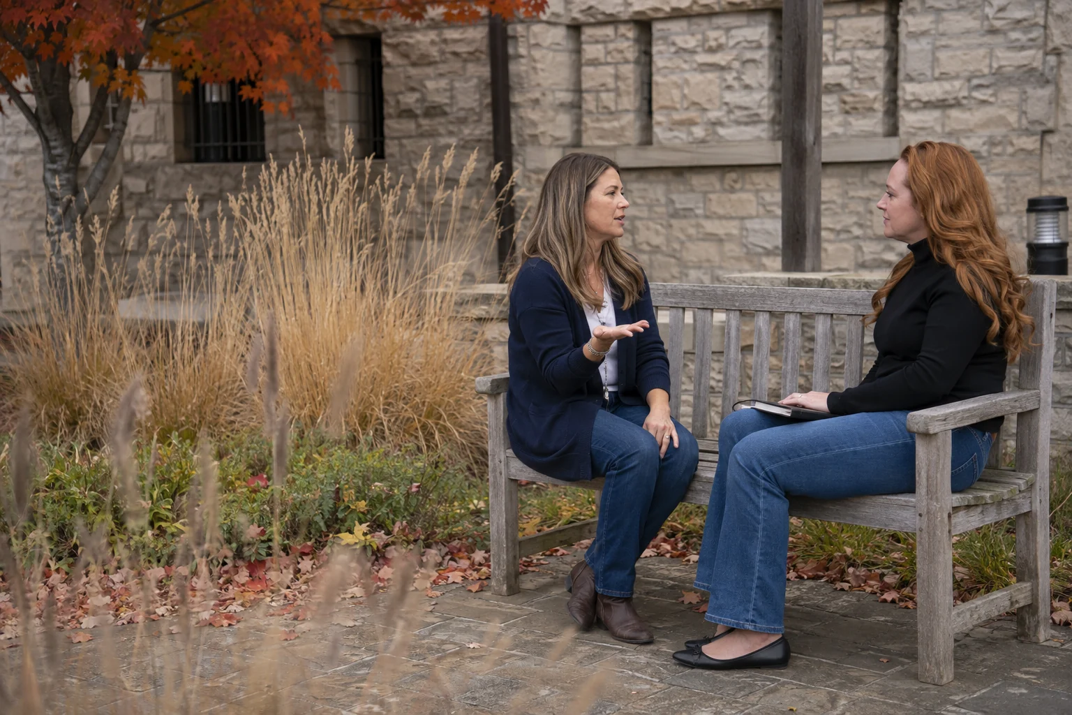 Samantha listening during a conversation on a bench in an autumn courtyard
